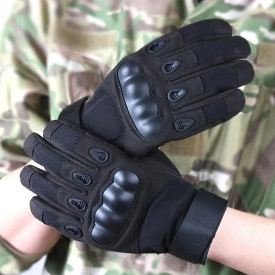 Black tactical gloves held in front of a camouflage background