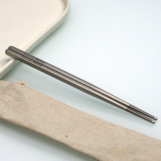 Pair of metallic chopsticks on a light surface with a fabric strip underneath